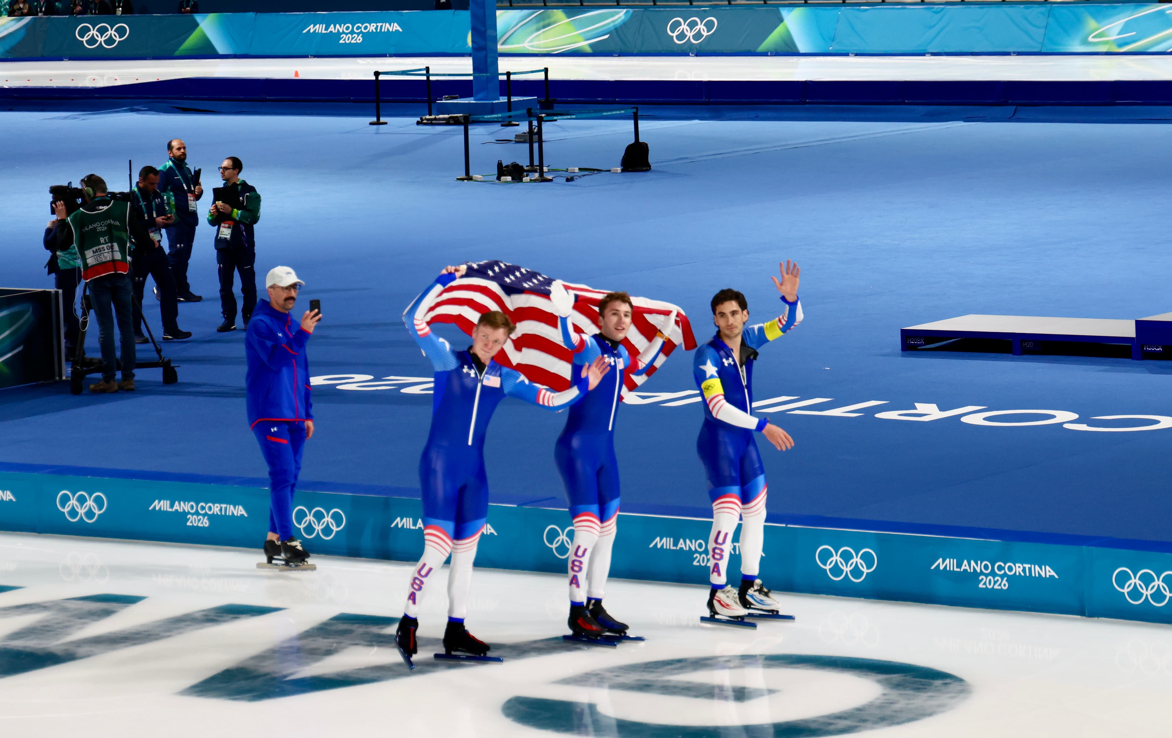 USA short track speed skating team celebrating with the American flag after their event at Milano Cortina 2026